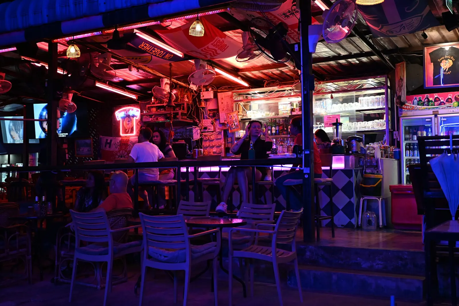 Bar iluminado em neon roxo e rosa, com gente no balcão