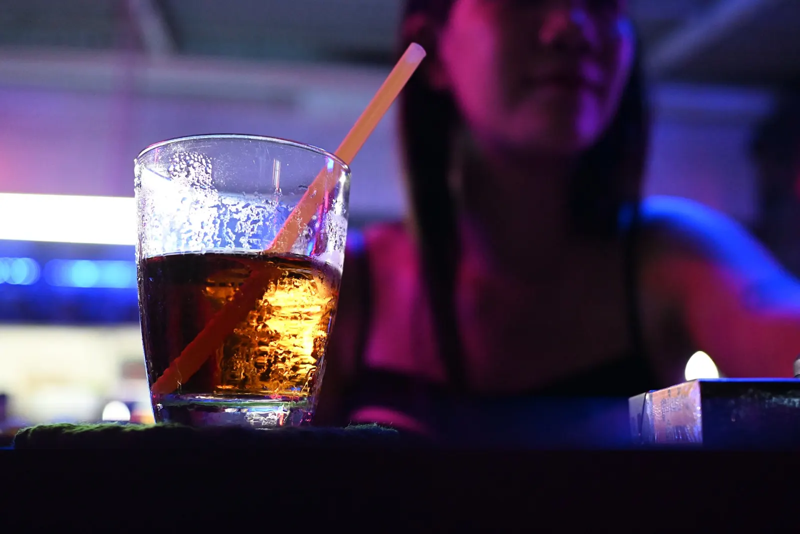 Copo de drinque no balcão sob luz neon azul e roxa